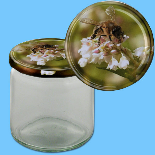 Das neutrale 500 g Honigglas mit einem runden TO-Metall-Deckel zeigt eine Biene auf einer Buchweizenblüte. Mit einem Durchmesser von 82 mm Ø eignet es sich hervorragend zur edlen Präsentation von Honig und bietet eine charmante, florale Darstellung.